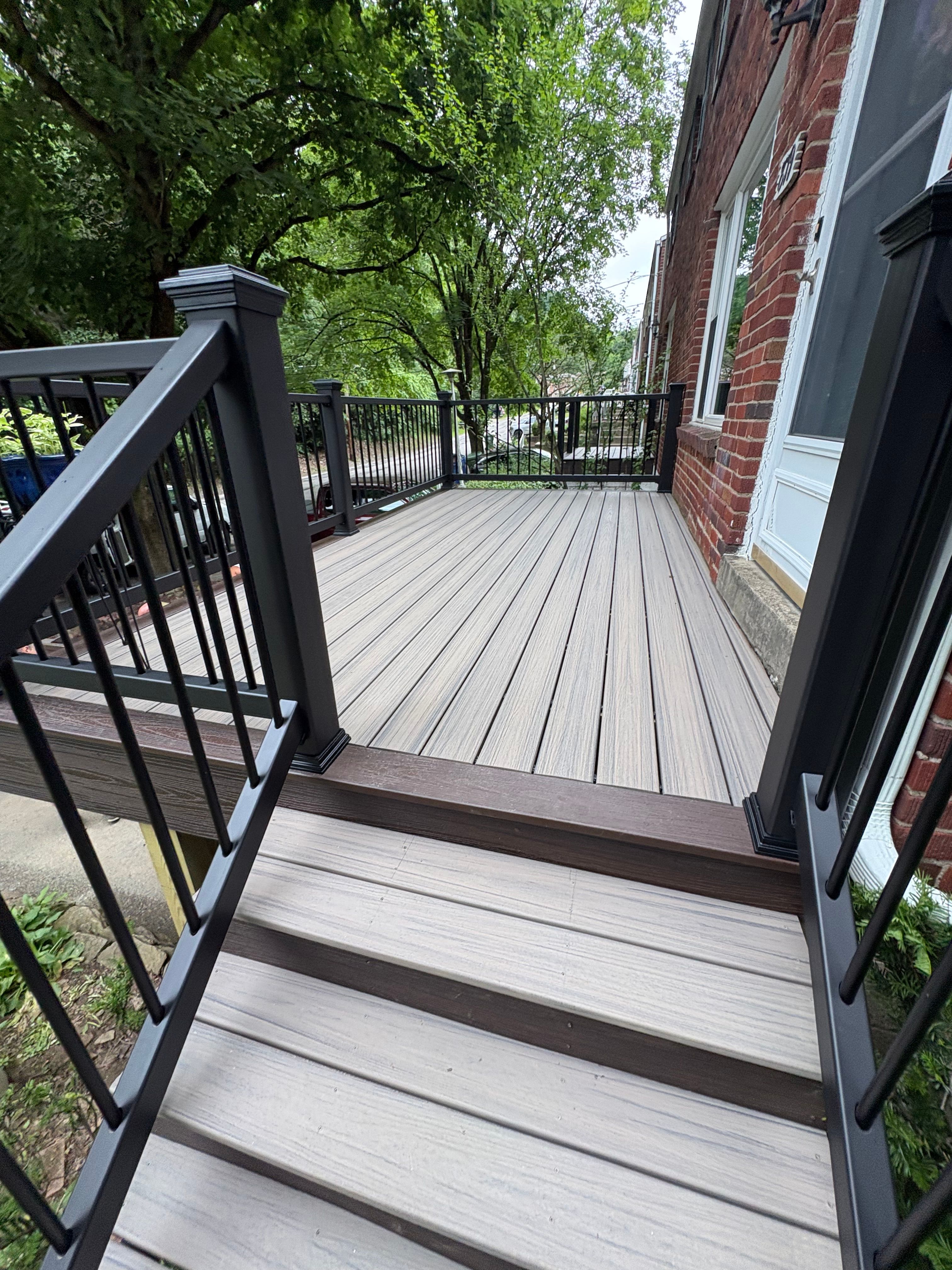 Grey composite deck with a dark border board and black railing beside a brick home
