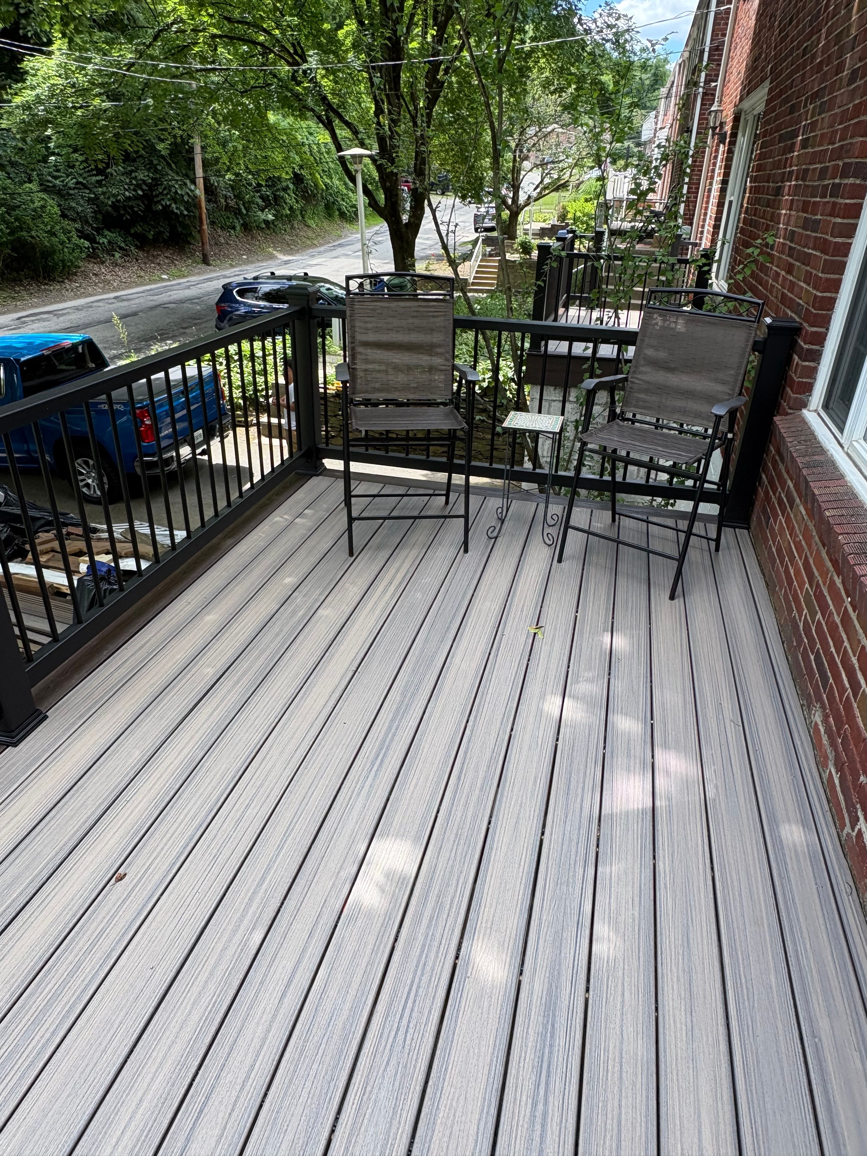 Grey composite deck with black railing and patio seating at a brick home