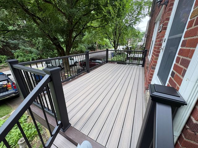 A grey composite deck with a black railing built off a brick house, under mature trees.