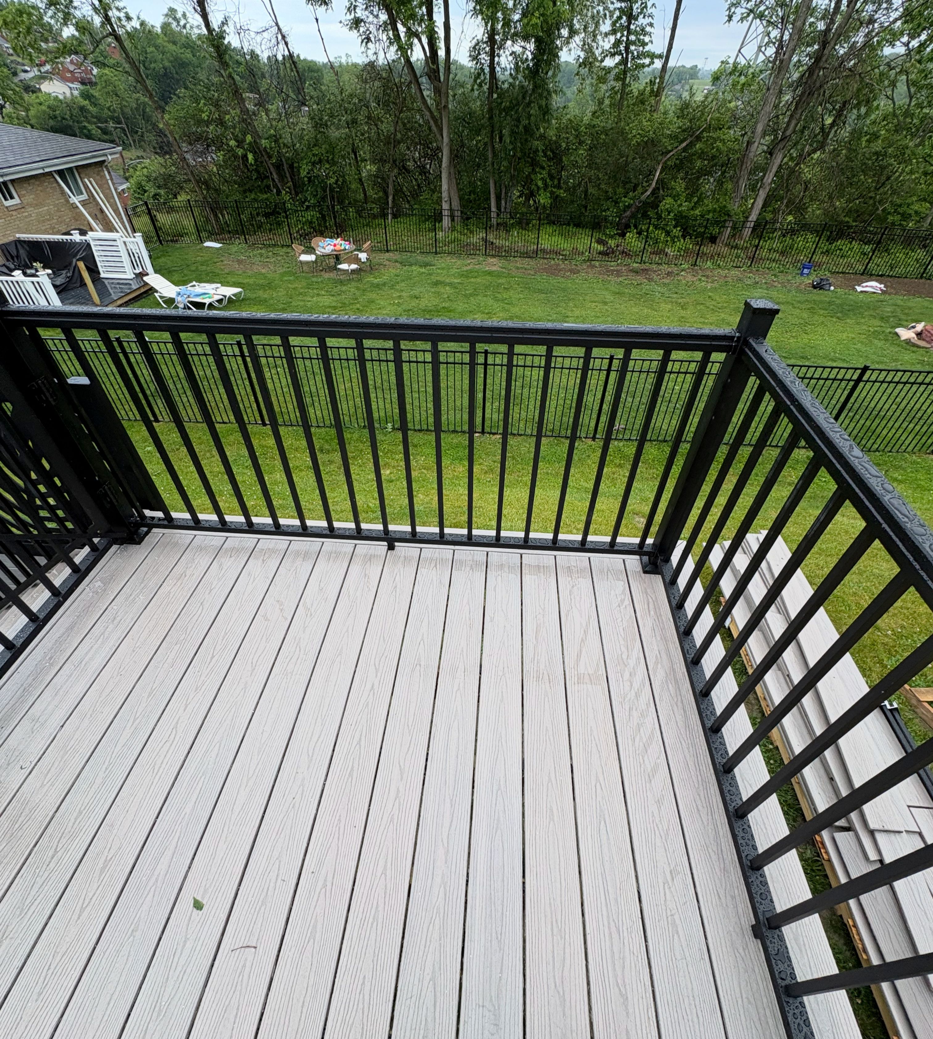 A composite deck with grey boards and a black aluminum railing, looking out over a mown lawn to a tree line.