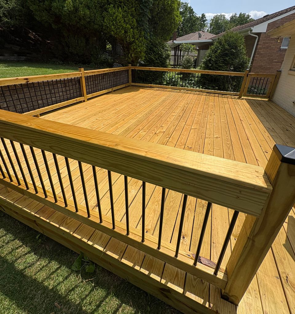 A newly built pressure-treated pine deck with a wood railing and black metal balusters, overlooking a fenced back yard.