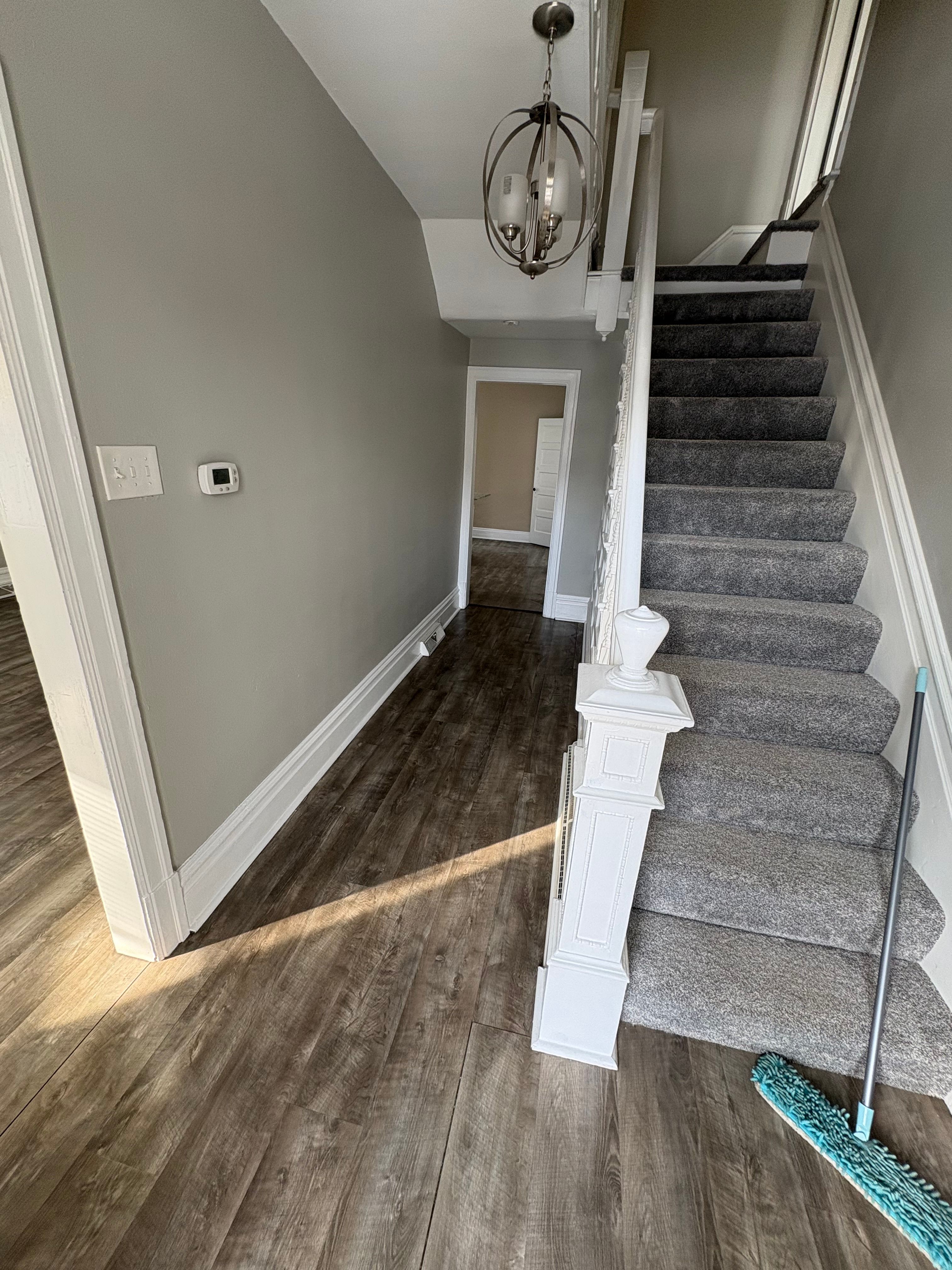 A remodeled entry hall with grey walls, dark wood-look plank flooring and a white staircase with carpeted treads.