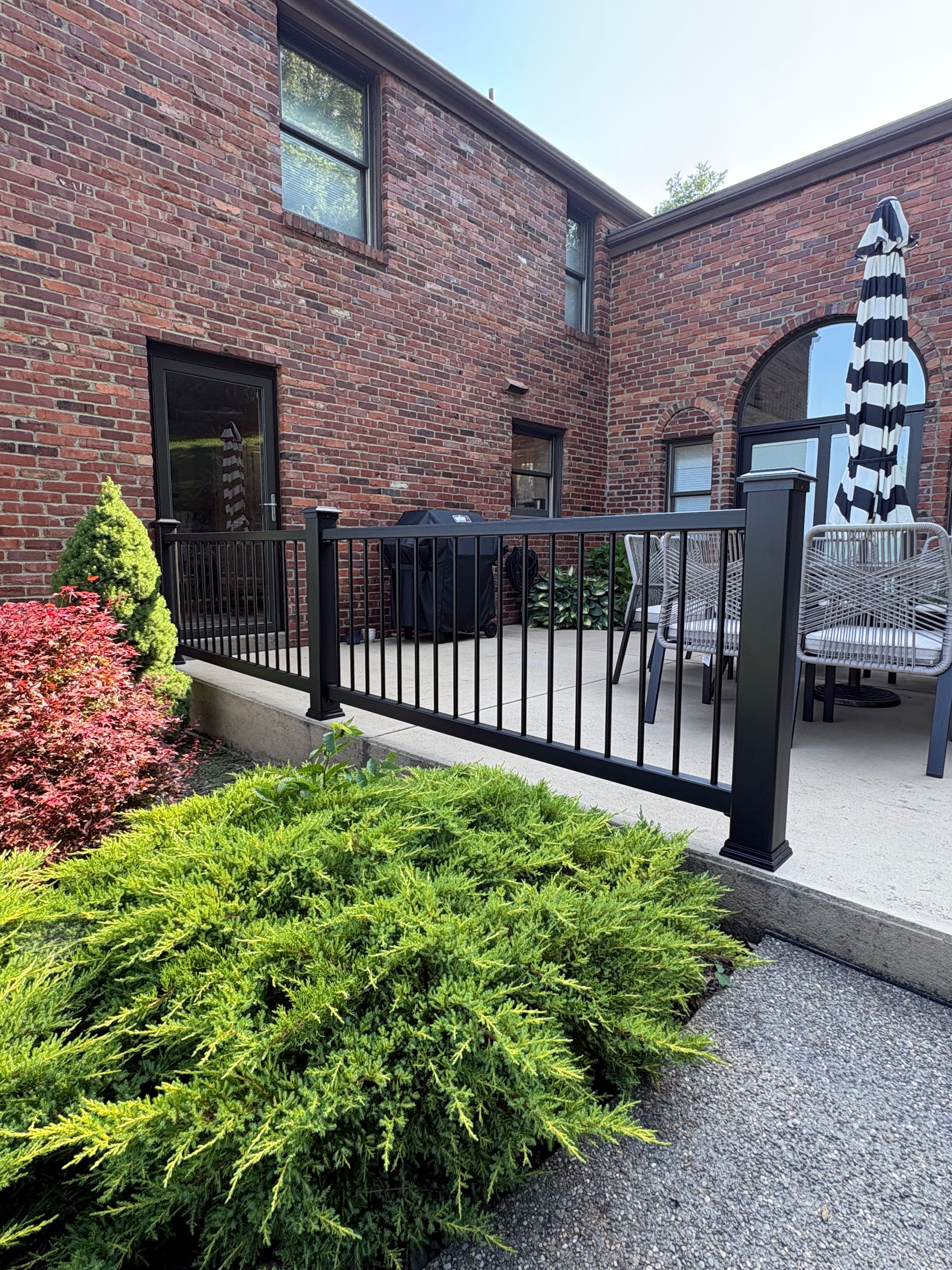 Black railing around a raised patio deck at a brick home