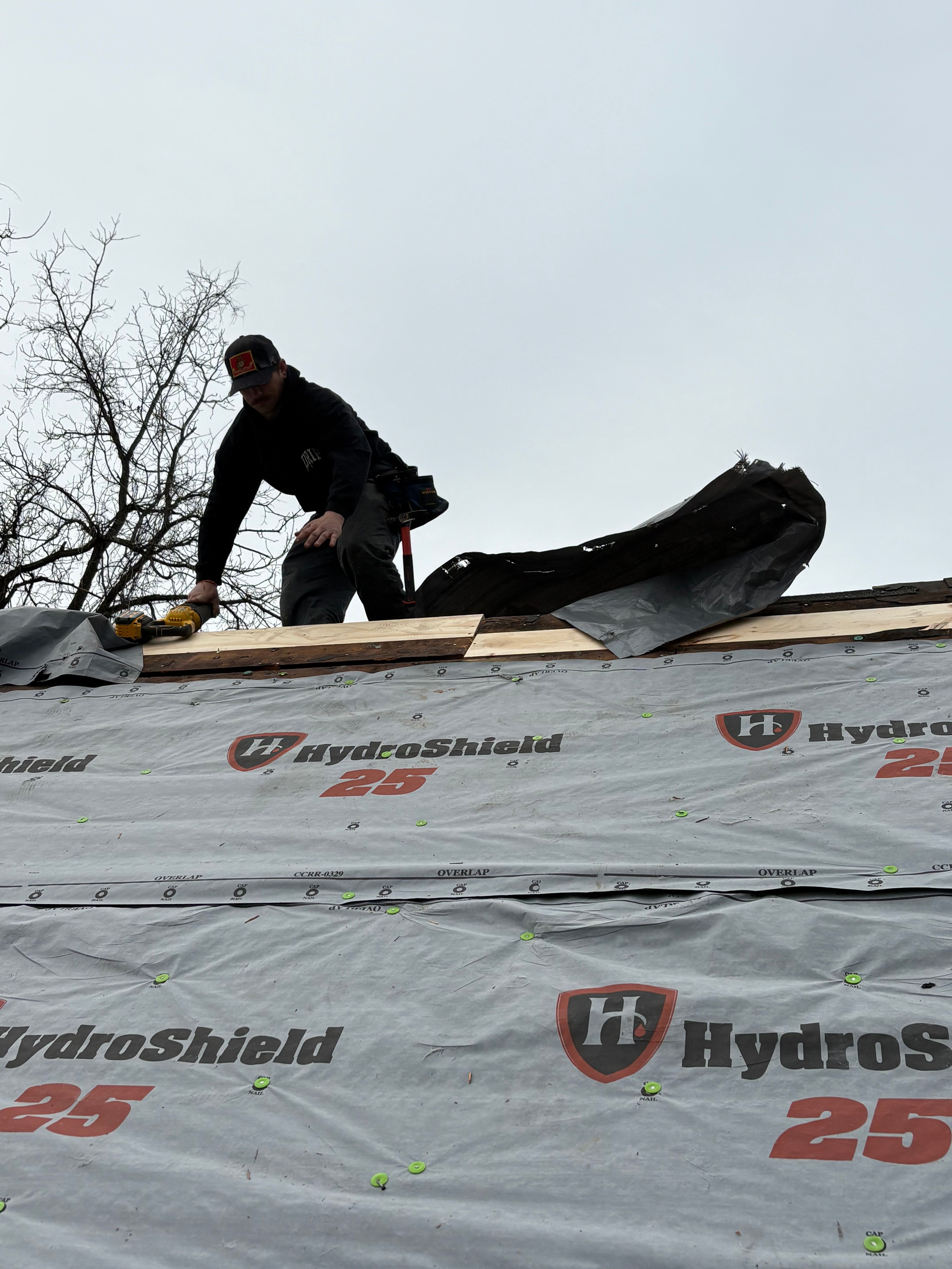 A roofer fastening board along a roof ridge over a freshly laid layer of synthetic underlayment.