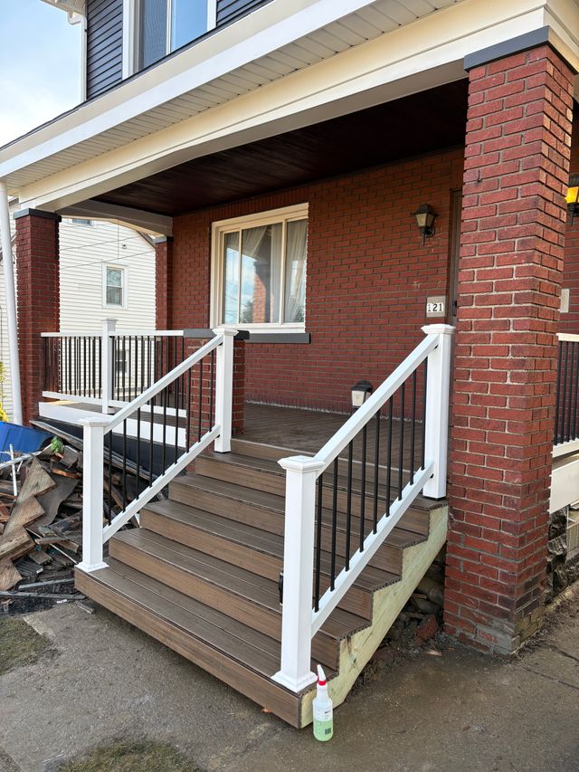 A rebuilt front porch on a brick house, with composite steps, a white railing and black balusters.